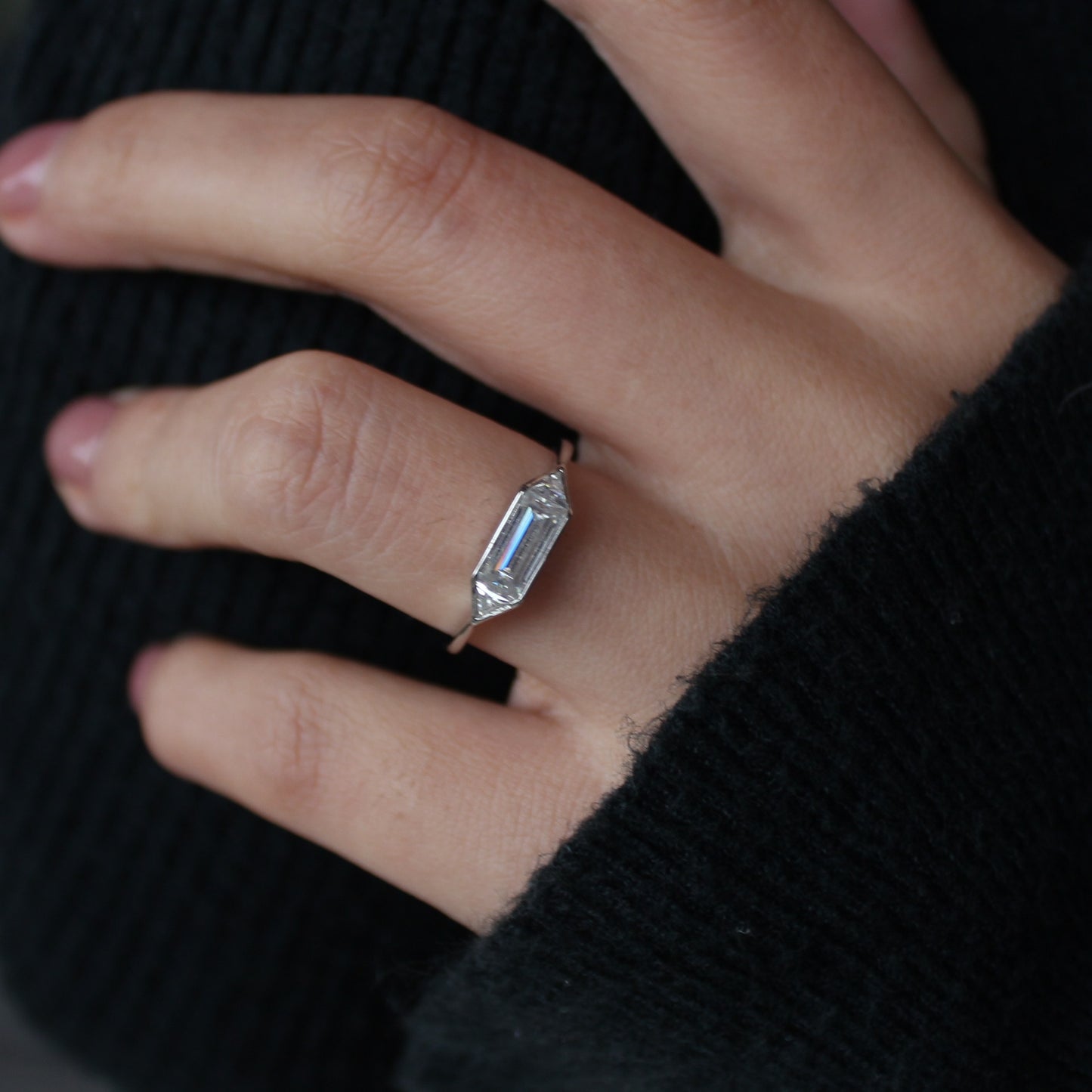 Emerald cut moissanite ring in bezel setting worn on hand, white gold tone