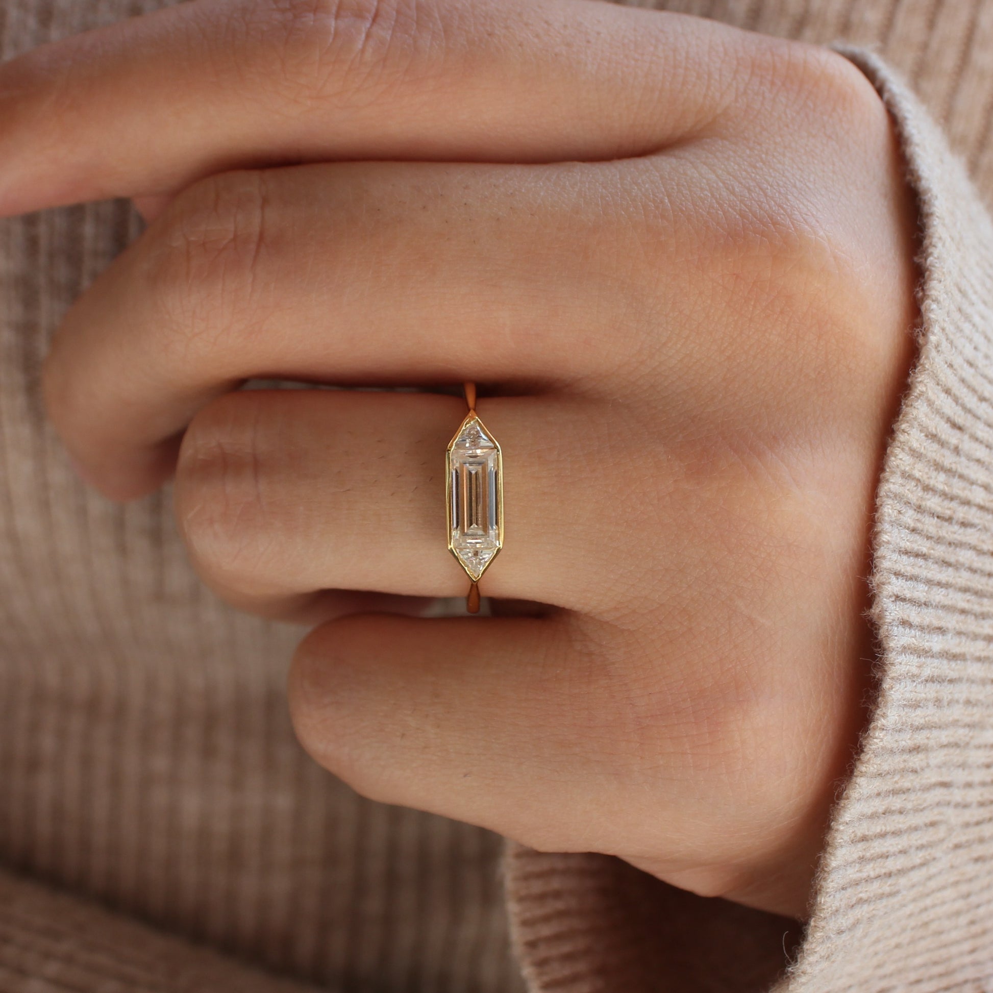 Emerald cut moissanite bezel ring worn on finger, minimal gold band
