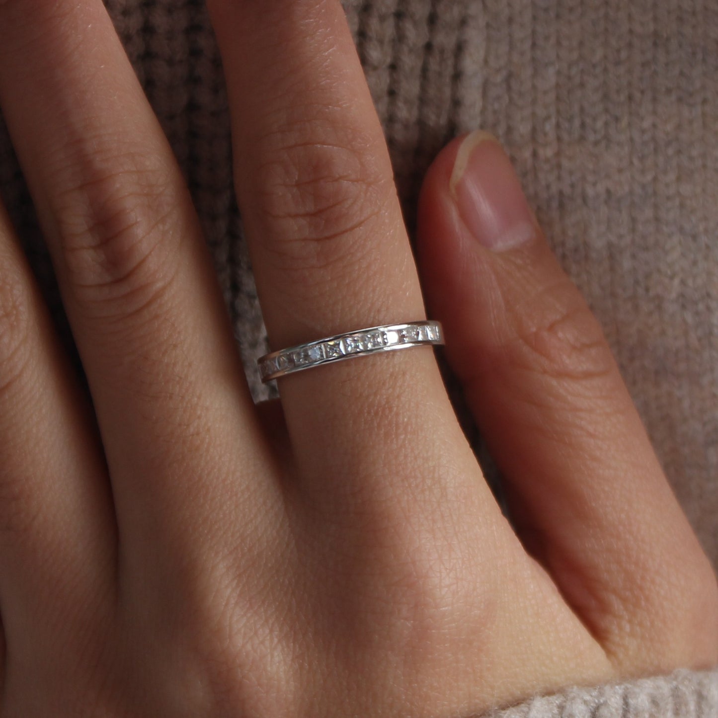 Close-up of baguette channel moissanite ring worn on finger, white gold tone finish