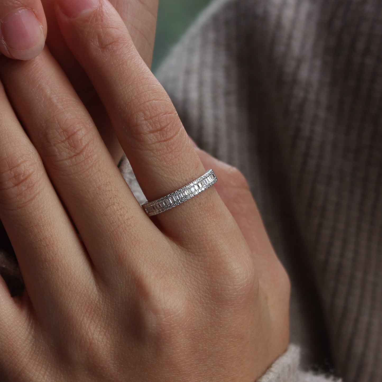 Close-up of baguette pavé moissanite band ring worn on finger, white gold tone finish