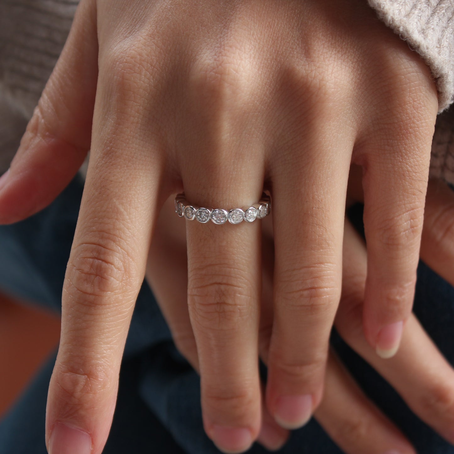 Close-up of bezel eternity moissanite ring worn on hand, white gold tone