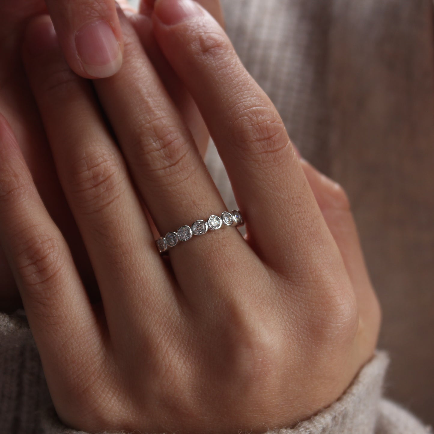 Bezel eternity moissanite ring on hand, white gold tone band with subtle sparkle