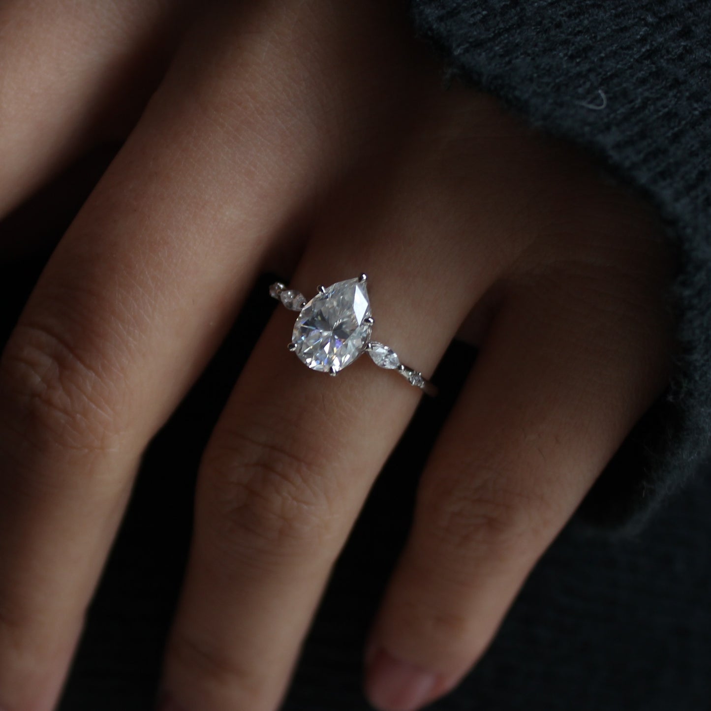 Elara pear moissanite ring shown on hand dark background