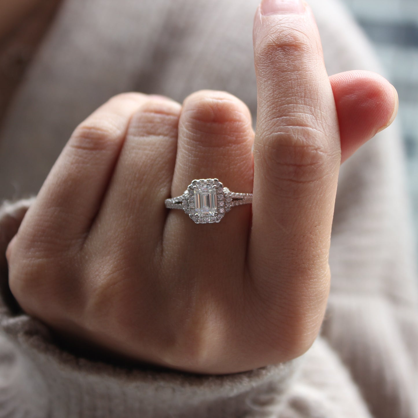 Close-up of emerald cut halo moissanite ring worn on finger, white gold tone finish
