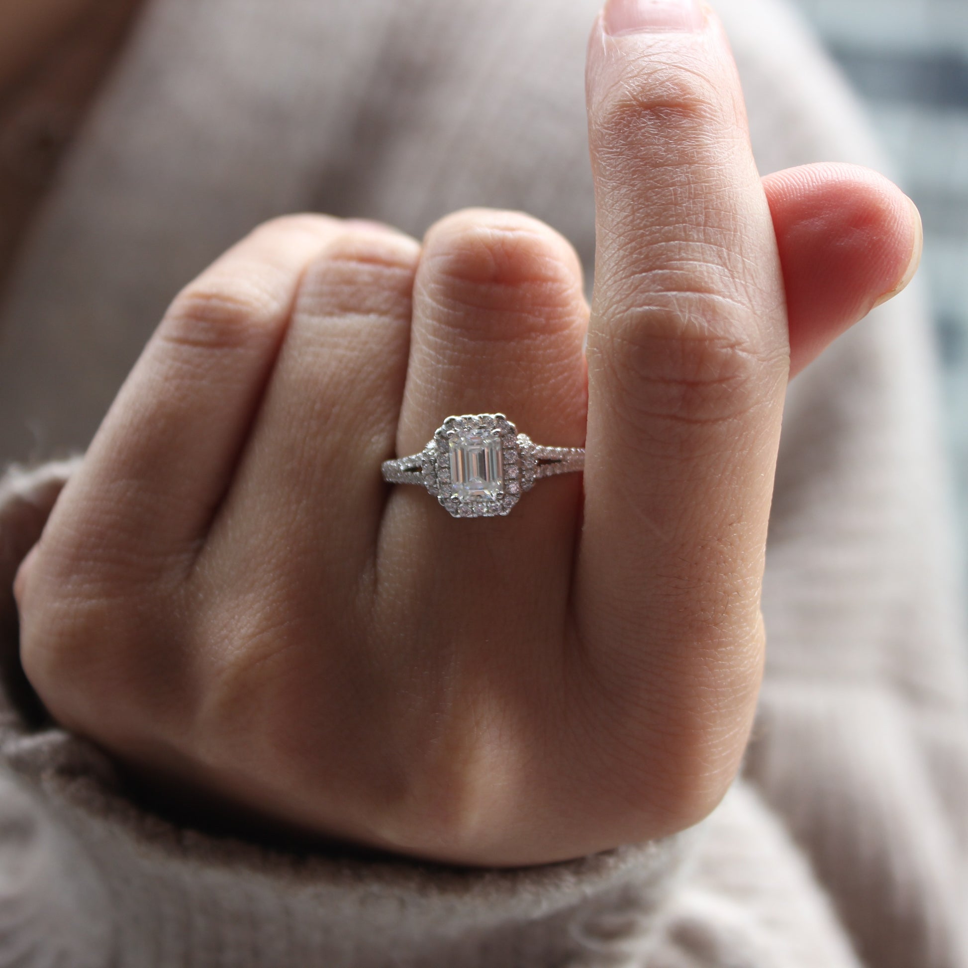Close-up of emerald cut halo moissanite ring worn on finger, white gold tone finish