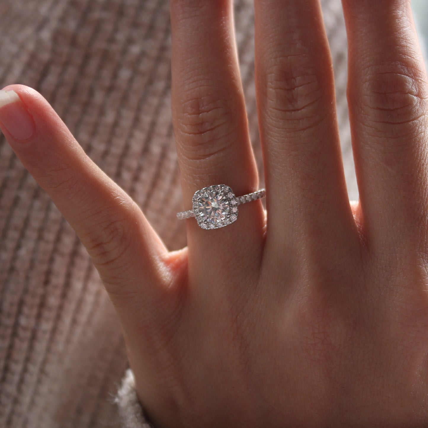 Close-up of halo pavé moissanite ring worn on finger, white gold tone finish