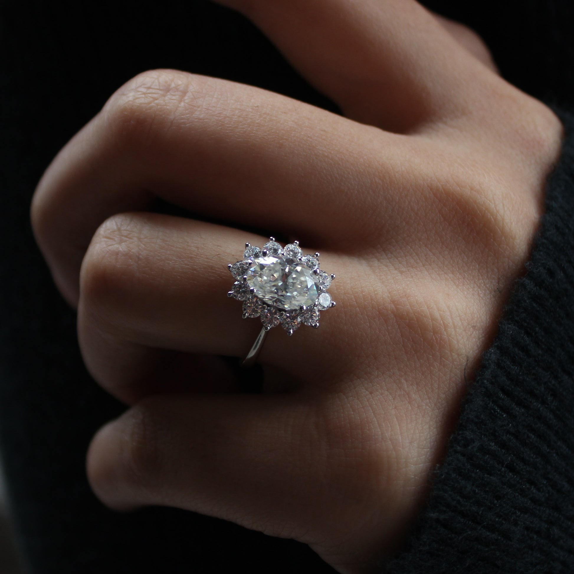 Oval moissanite halo ring worn on finger, dark background